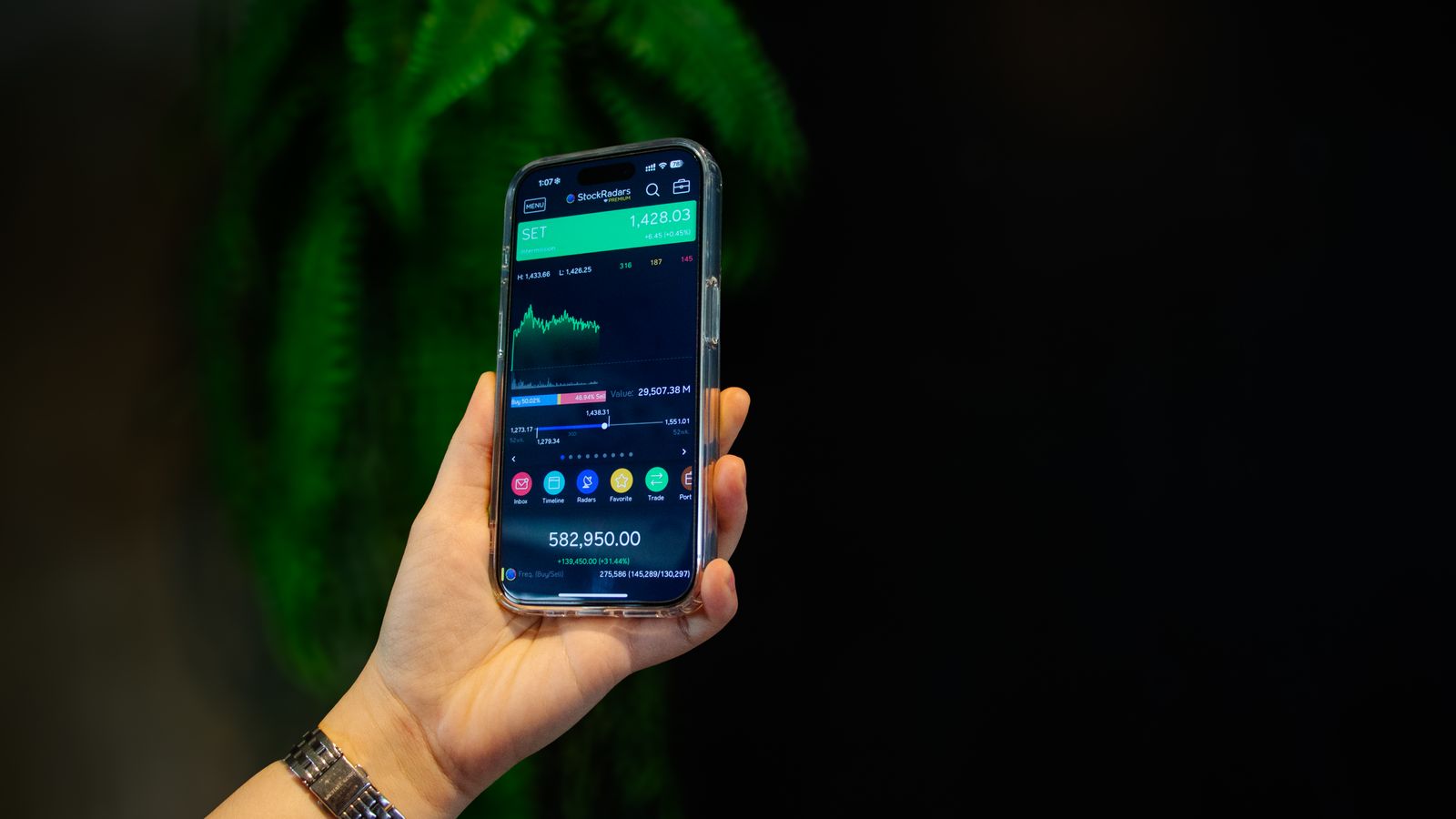 Tangan memegang ponsel yang menampilkan aplikasi trading saham.