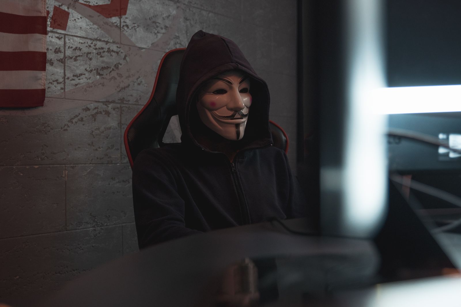 Sosok mengenakan hoodie meretas komputer dalam ruang gelap, ilustrasi peretas negara